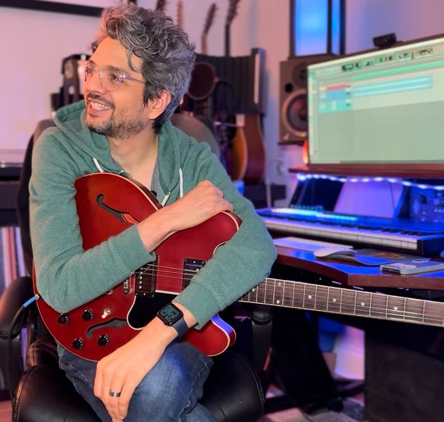 Alternative rock and metal producer J.K. Royston sitting in a studio with a guitar
